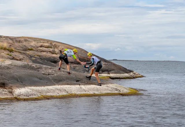 swimrun-deltagare på väg upp ur vattnet på bergknall