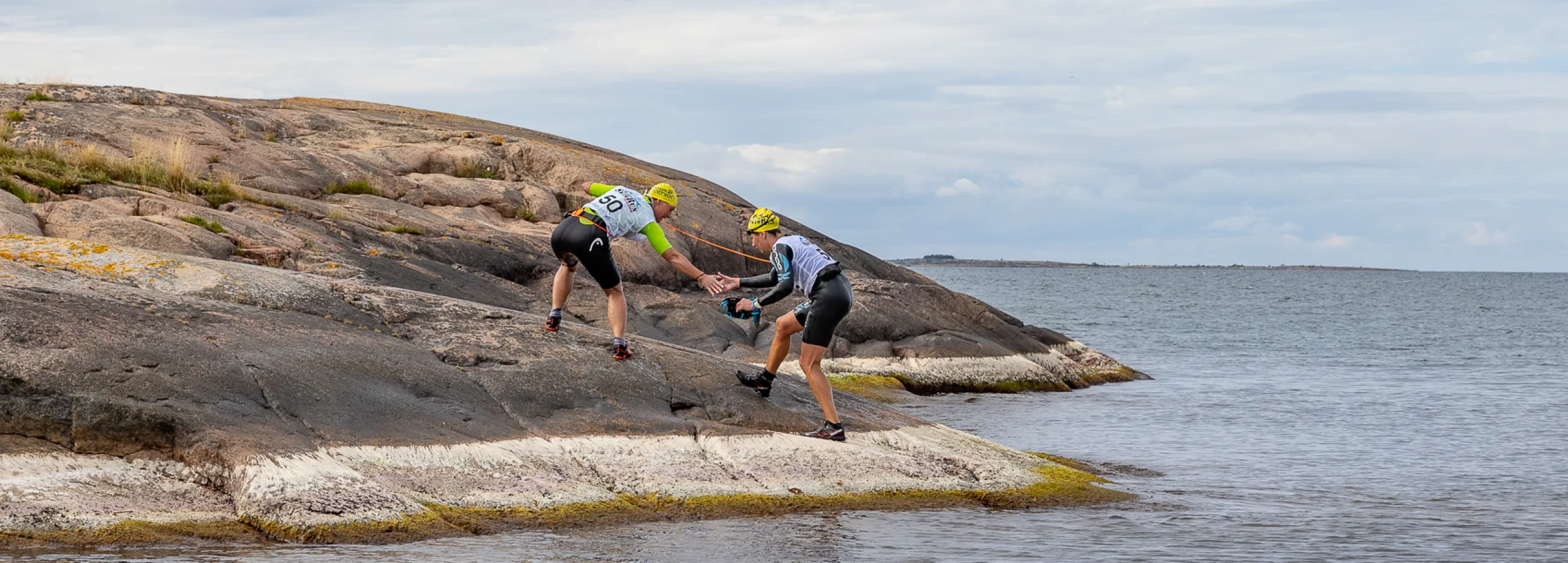 swimrun-deltagare på väg upp ur vattnet på bergknall