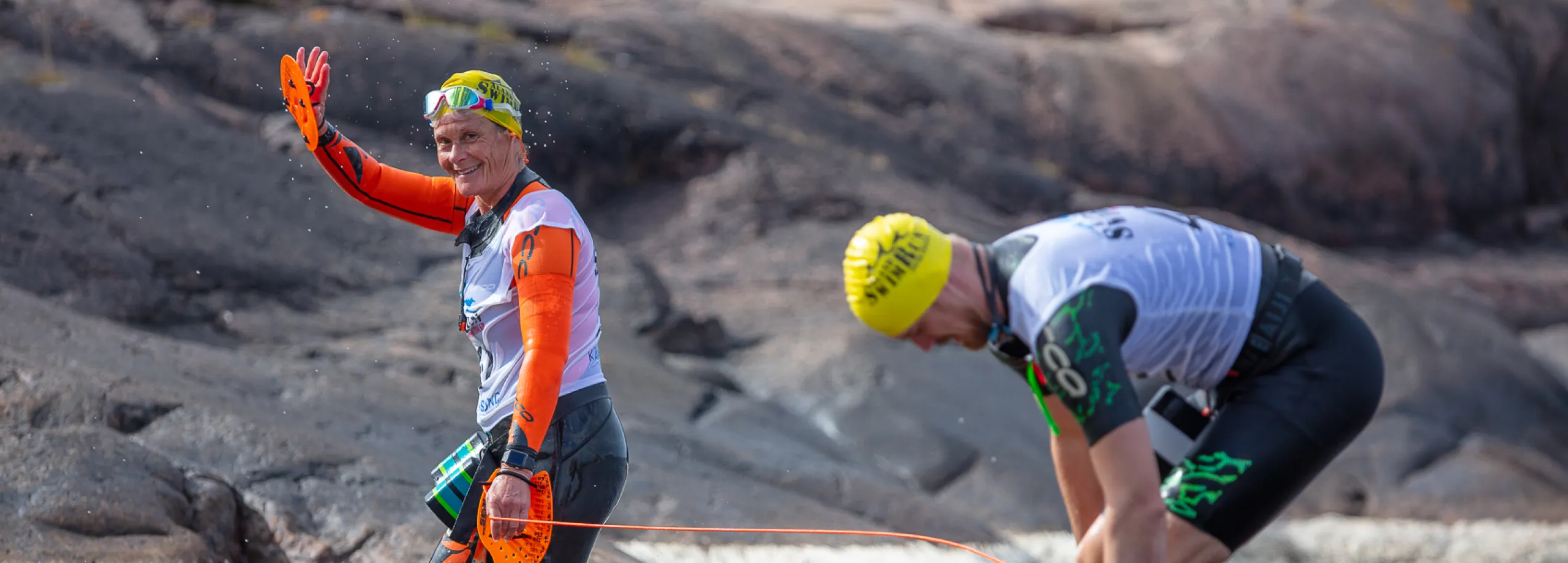 två swimrun-deltagare just uppkomna ur vattnet ståendes på en klippa