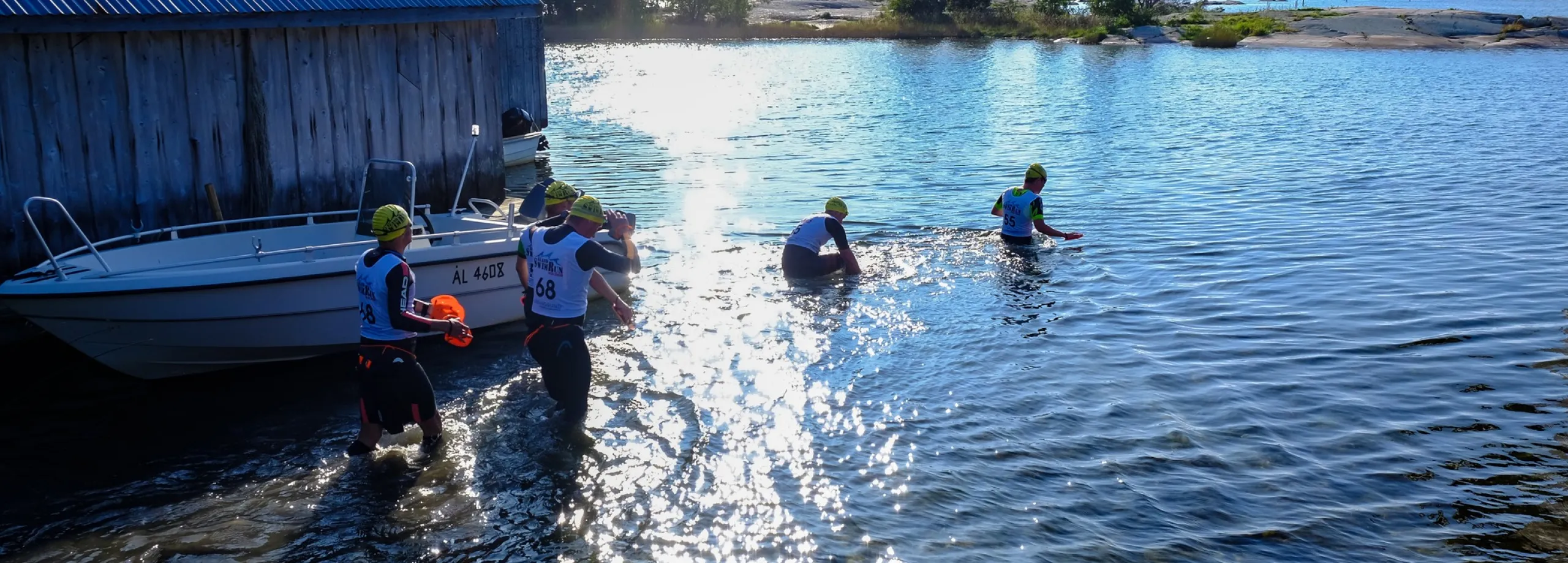 swimrun-detagare går i vattnet vid sjöbod